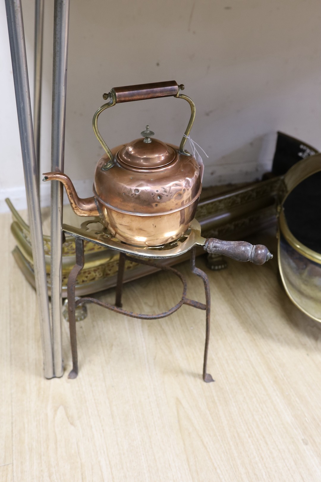 A copper kettle and trivet stand, a brass coal scuttle and a fender, Trivet 33 cms high.